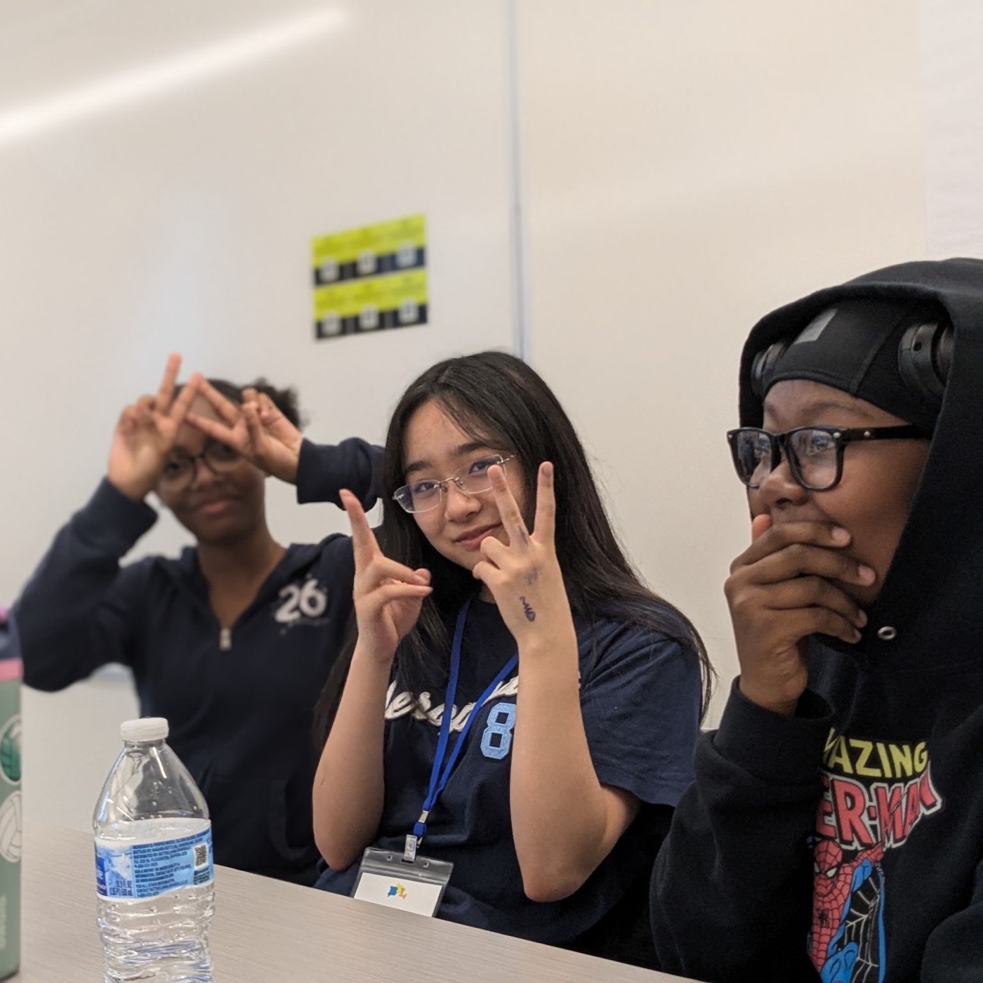 Three campers smile and flash peace signs while sitting together at a table.