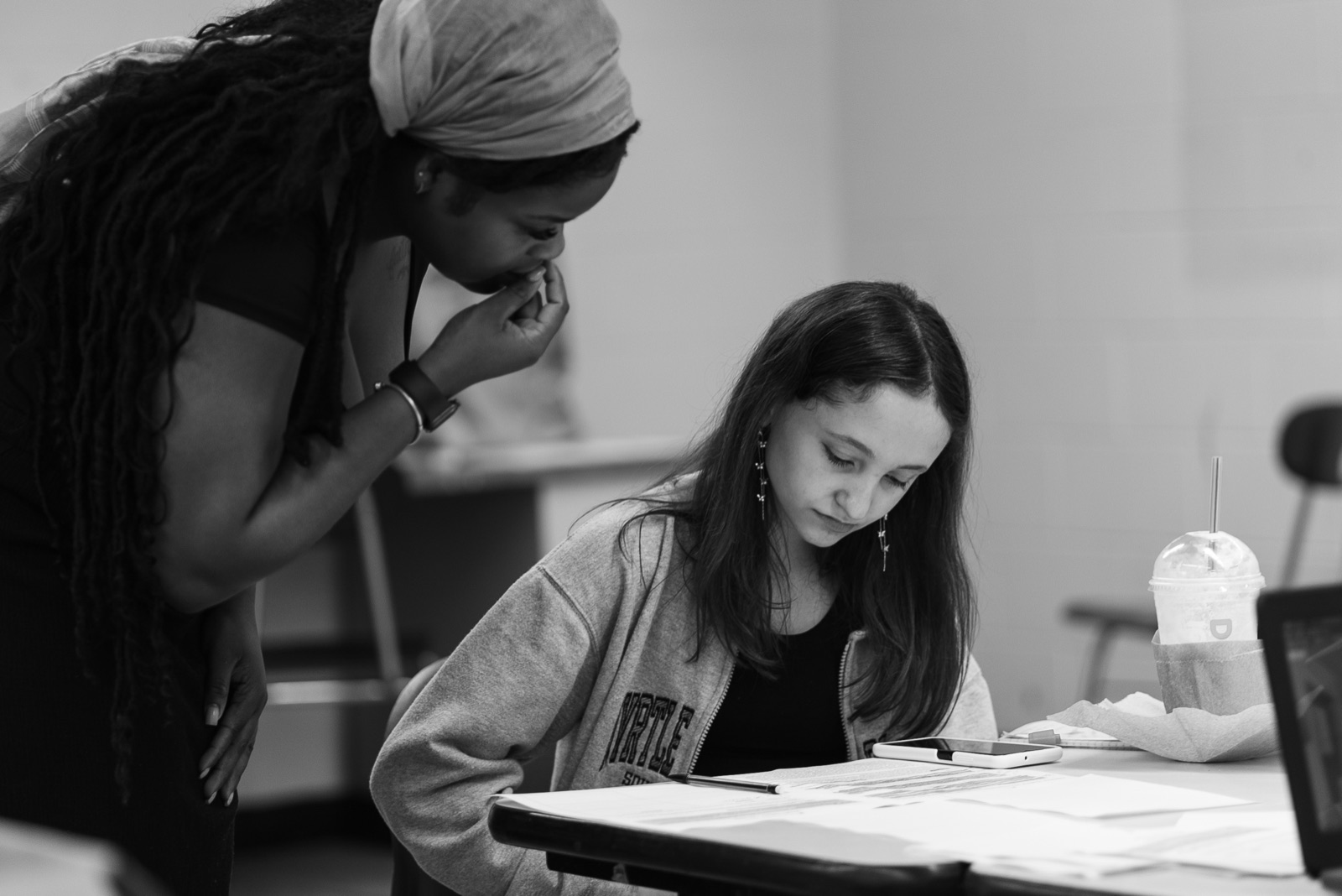 A camp educator leans in to support a student working at a table.