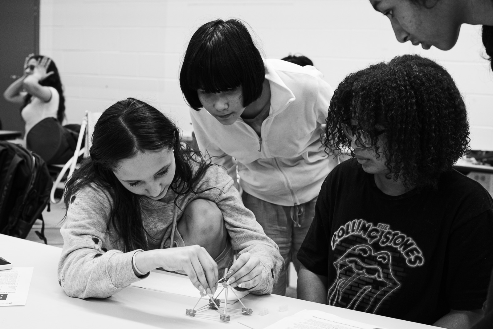 Three campers lean over a table and collaborate on a small building challenge.
