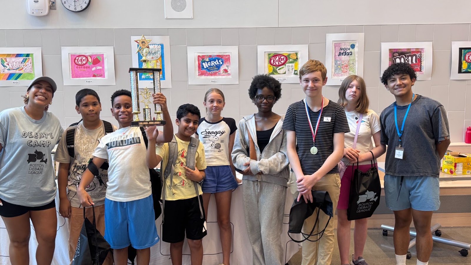 A group of campers and a coach pose together with a large debate trophy.